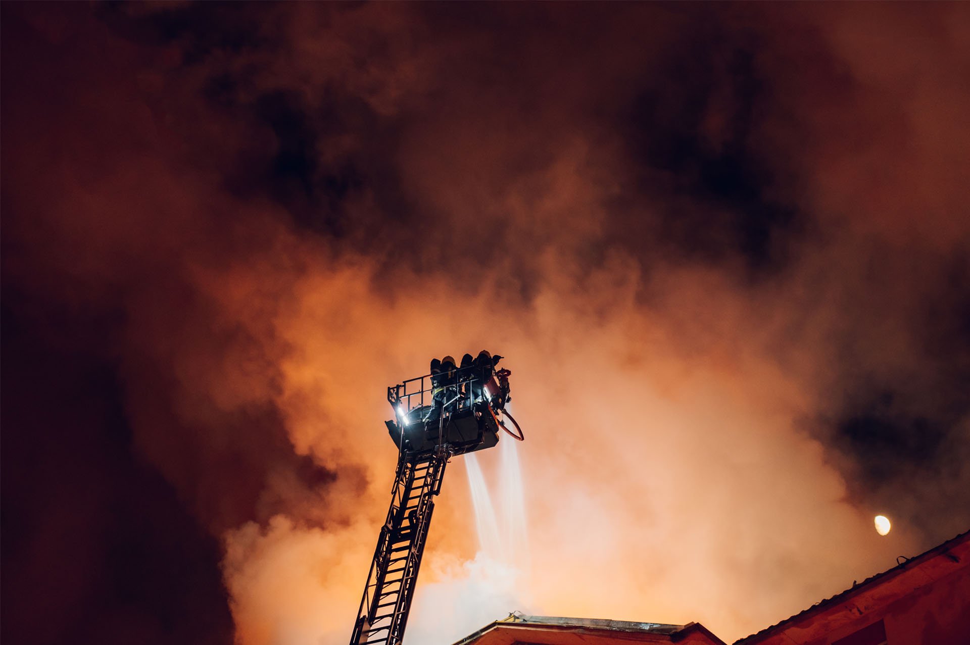Fire Fighters on a ladder extinguishing a rooftop building fire likely caused by not following NFPA guidelines.